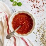 Red thin sauce in a small white bowl with a spoon.
