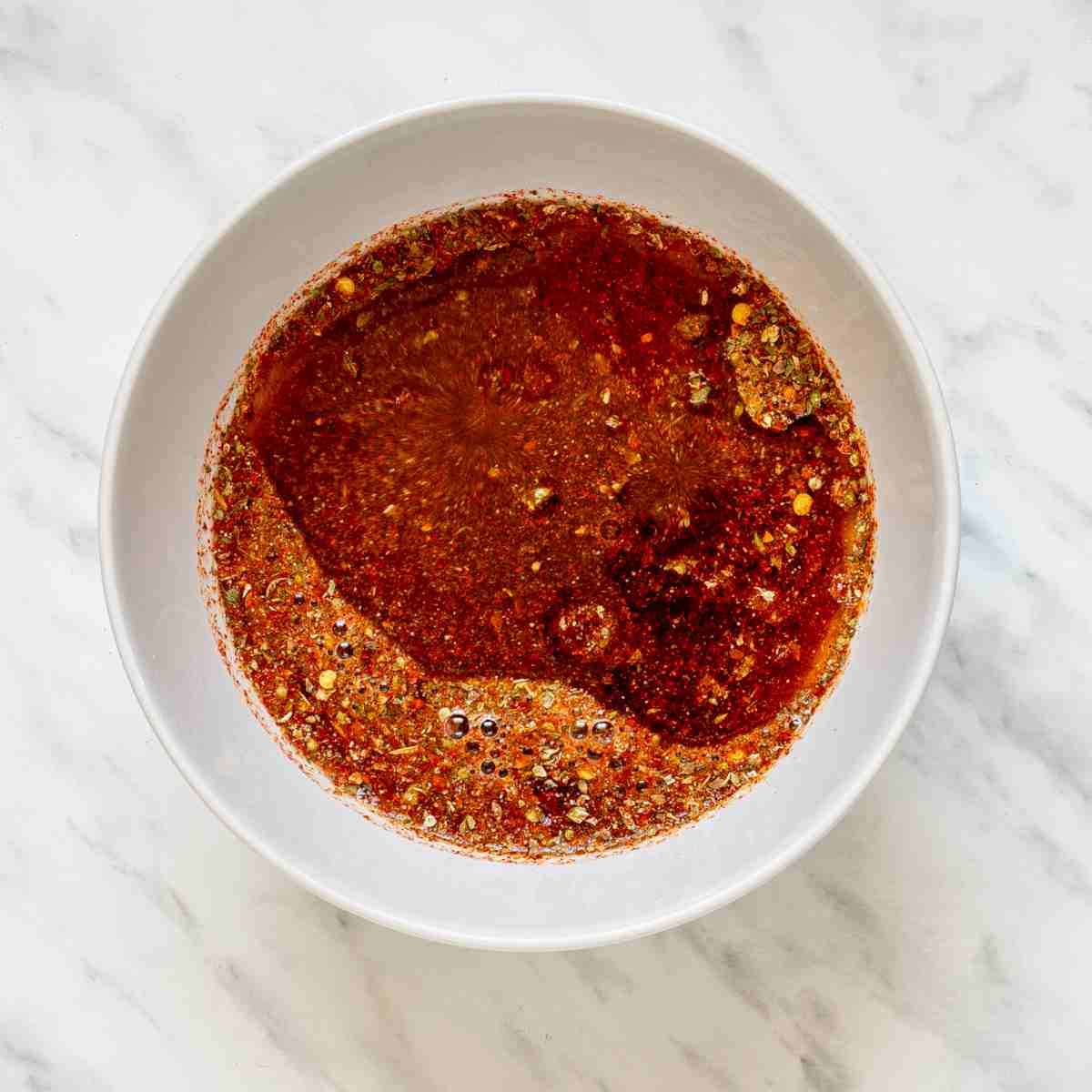 Mix of liquid ingredients and a red spice mix in a small white bowl.