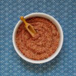 Small white bowl with a red spice mix and a small wooden spatula.