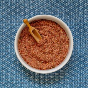 Small white bowl with a red spice mix and a small wooden spatula.