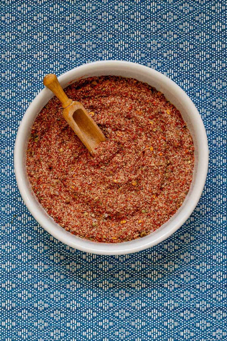 Small white bowl with a red spice mix and a small wooden spatula.