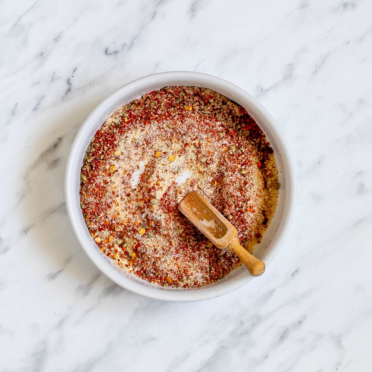 A white bowl with a small wooden spatula and a mix of spices.
