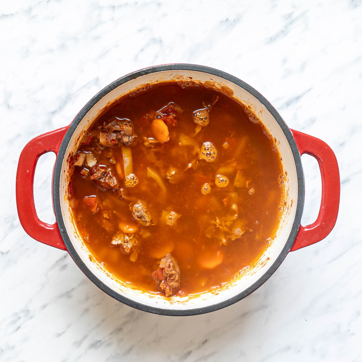Broth in a pan with meat and vegetable mixture to make Hungarian goulash.