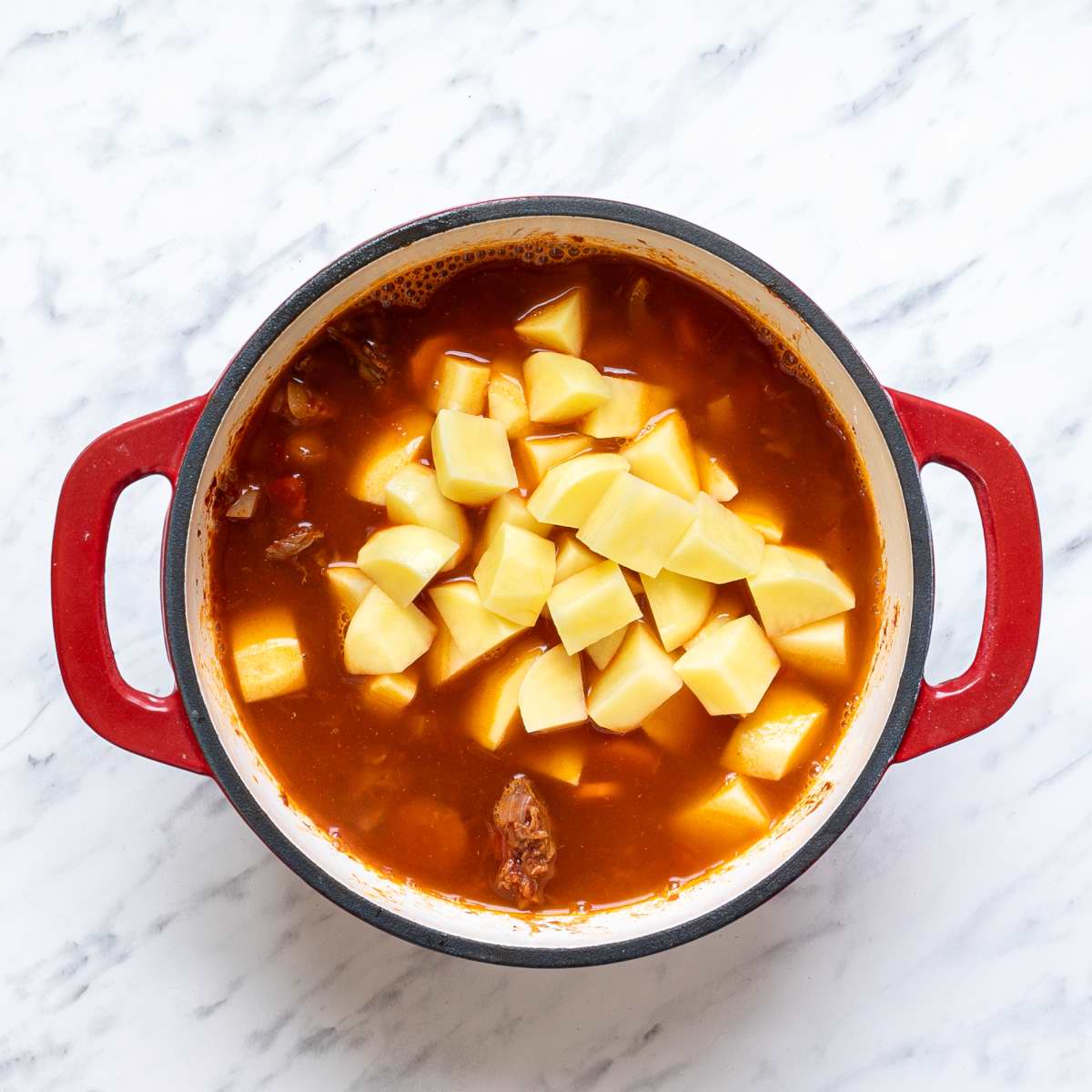 Chopped potatoes in a pot with vegetable broth and meat mixture to make Hungarian goulash.