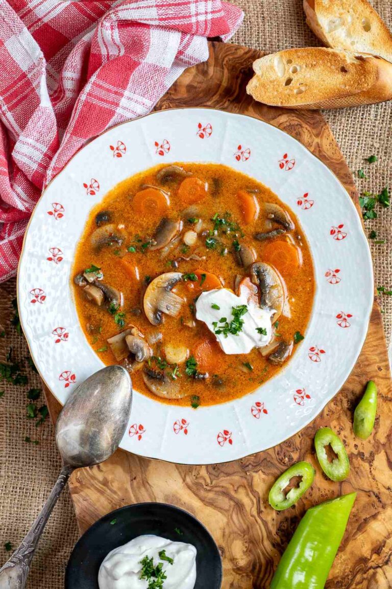 A bowl of Hungarian mushroom soup with sour cream on a wooden cutting board.