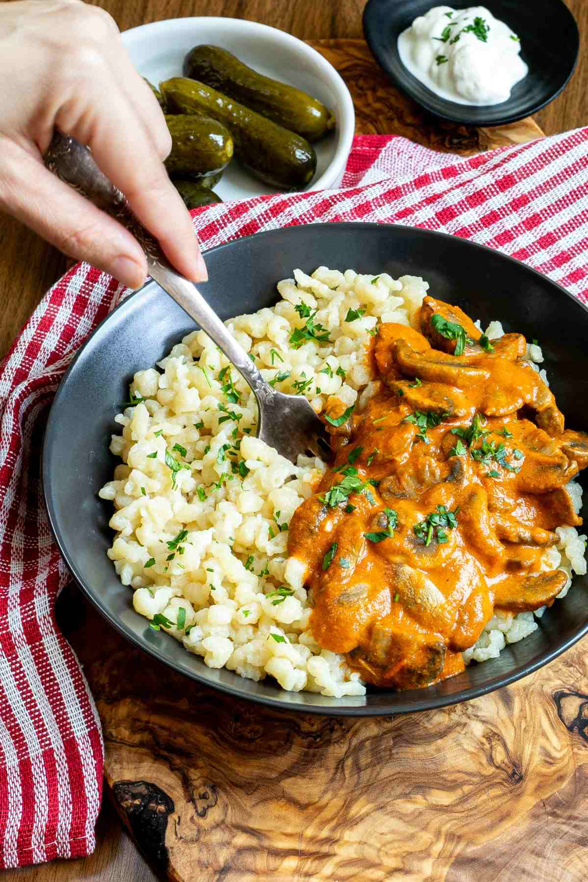 A person holding a fork in a bowl of Hungarian mushroom stew over nokedli.