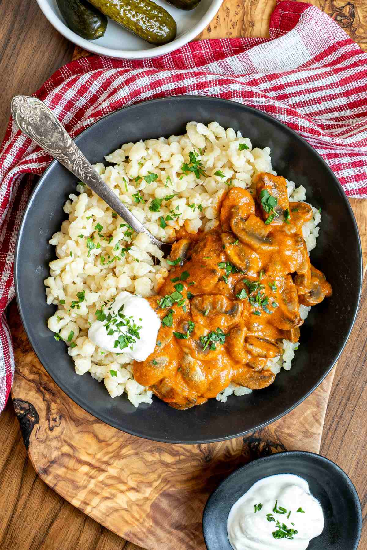 Overhead shot of Hungarian mushroom stew over nokedli in a black bowl with sour cream.