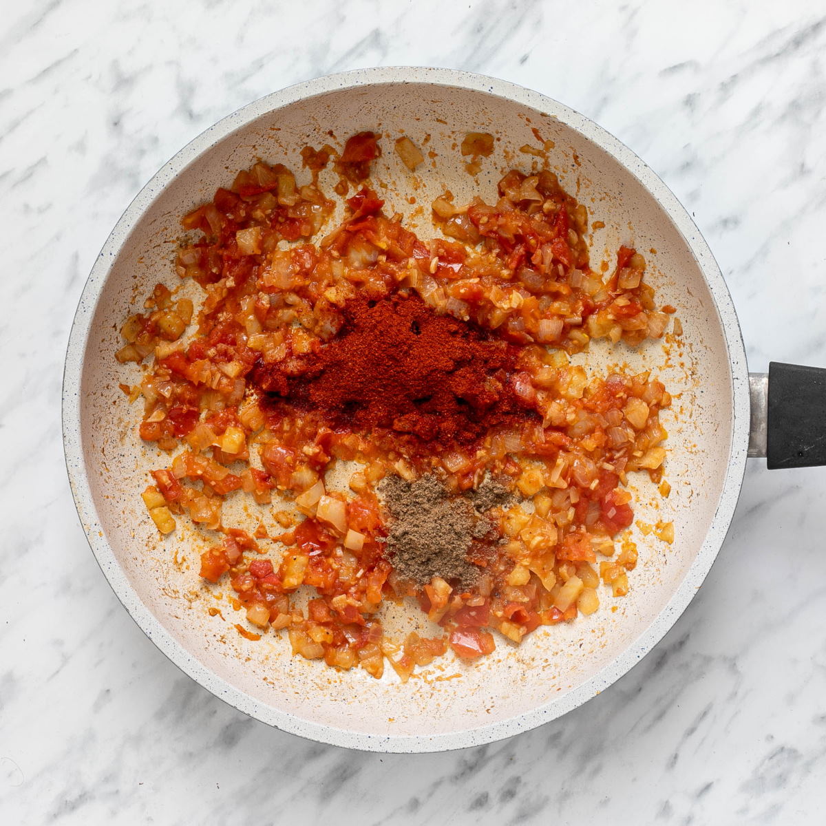 Sauteed onion with spices on top in a white frying pan. 