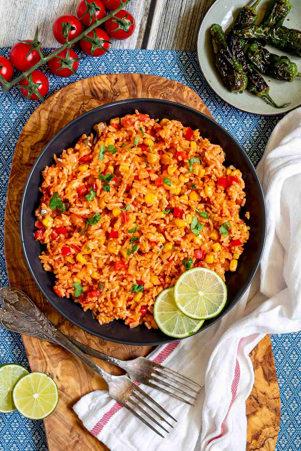 Orange rice with corn, tomato, and parsley in a black bowl. Lime slices are on the side.
