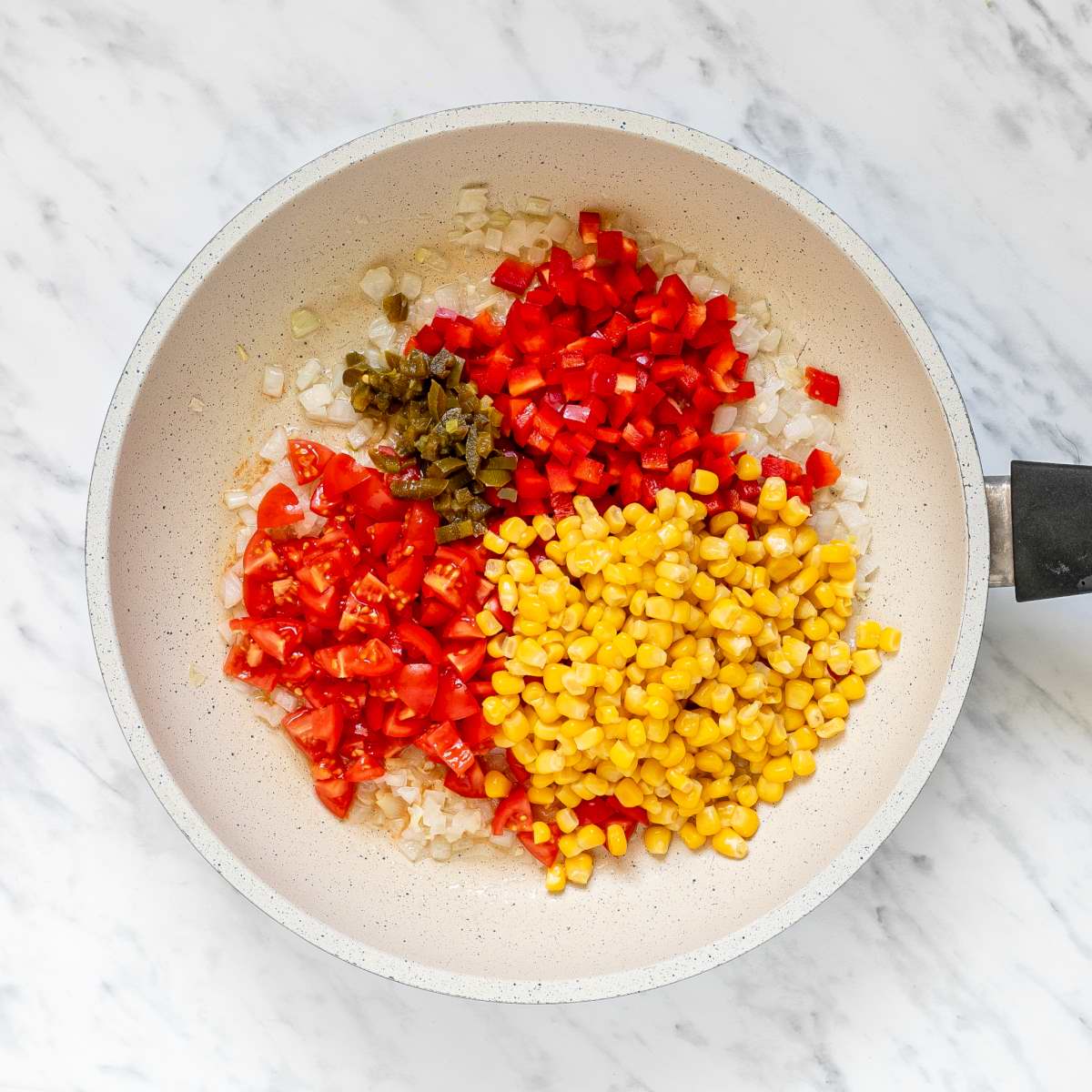 White frying pan with chopped tomatoes, bell peppers, corn and green chilies.