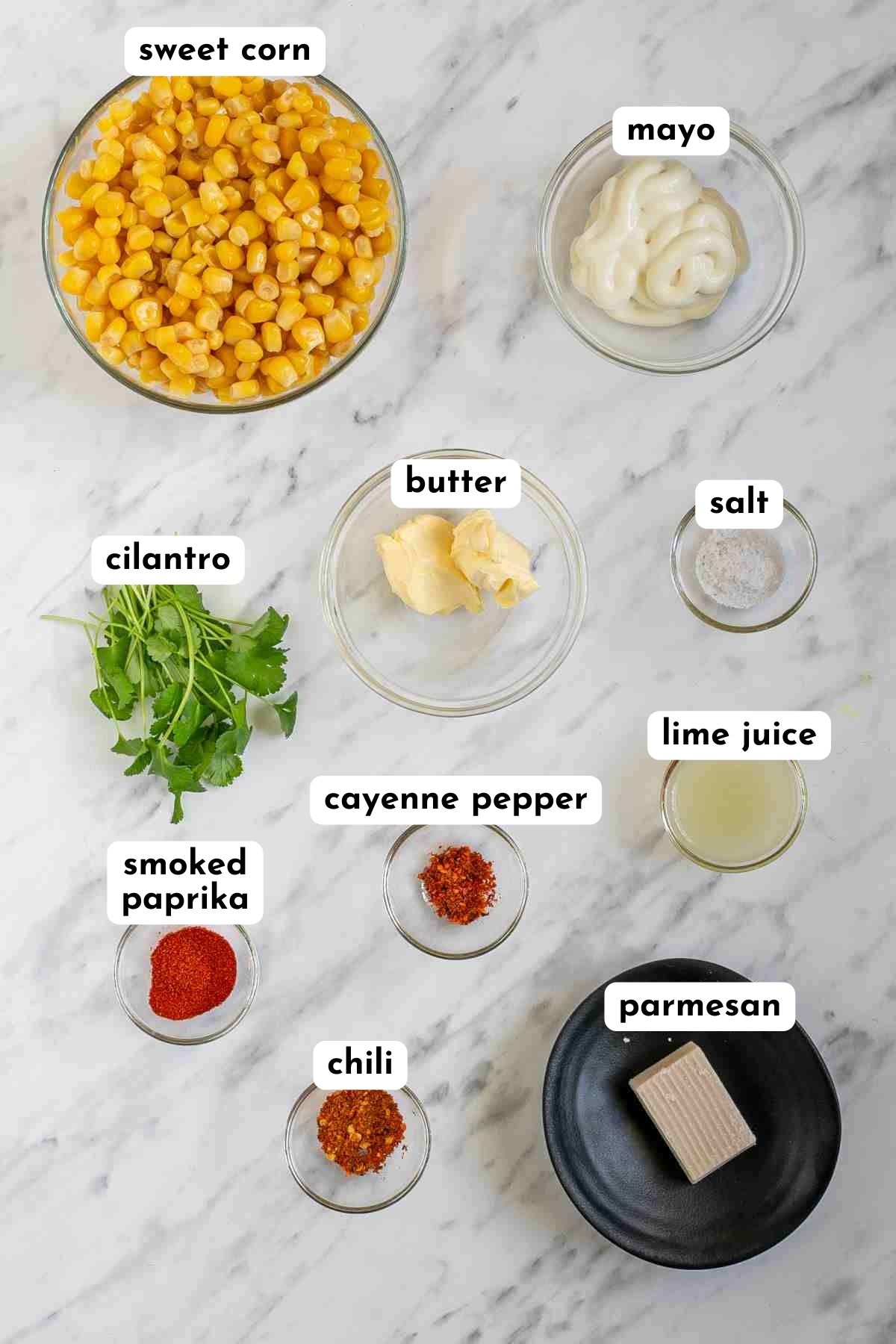 Ingredients of mexican street corn in glass bowls like yellow corn kernels, butter, cilantro, parmesan, red paprika powders and salt