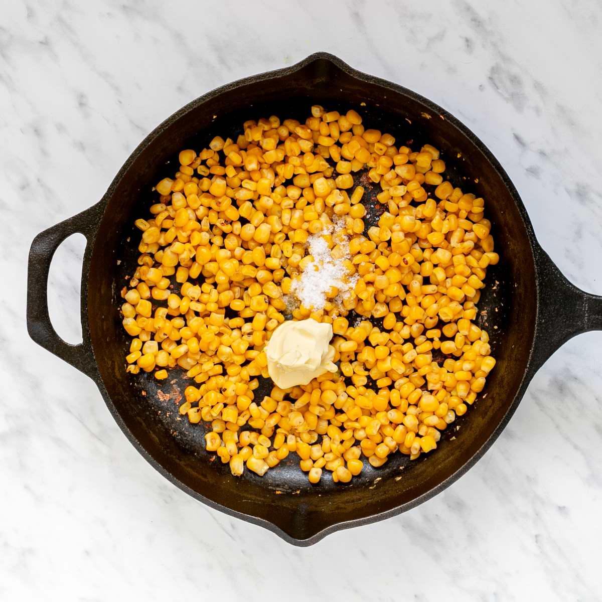 Cast iron skillet full of slightly charred yellow corn kernels and a scoop of butter and and a small heap of salt.