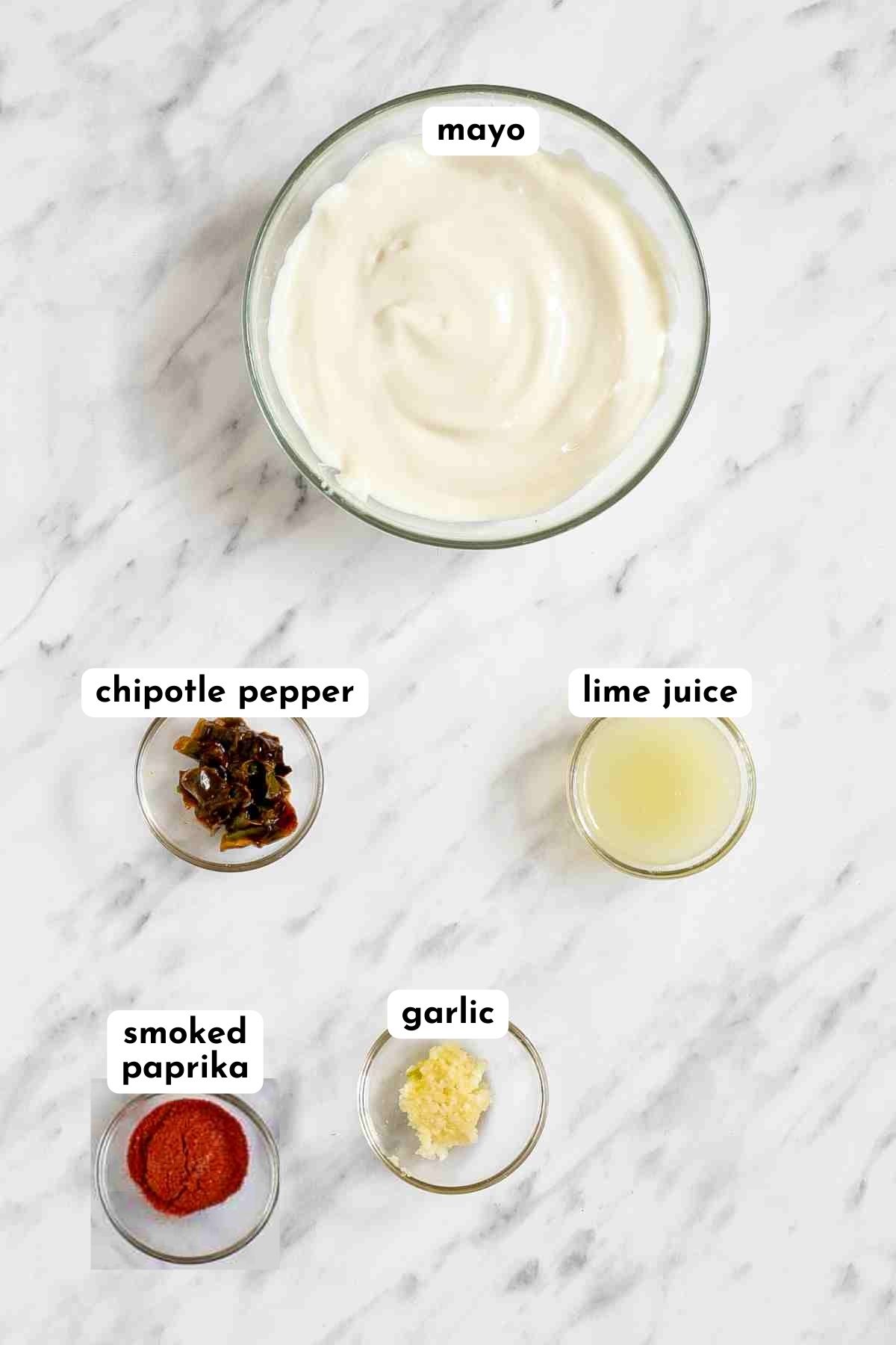Ingredients of vegan chipotle mayo in small glass bowls like mayo, finely chopped peppers, paprika powder, lime juice, and minced garlic.
