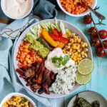 White bowl with cilantro lime rice, corn salsa, mushroom fajitas, guacamole, fajitas veggies and chipotle mayo.