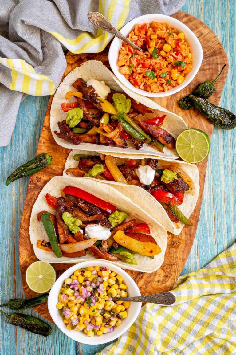 Small tortillas with colorful pepper slices and crispy brown mushroom shreds topped with white and green sauces on a wooden board. Surrounded by side dishes.