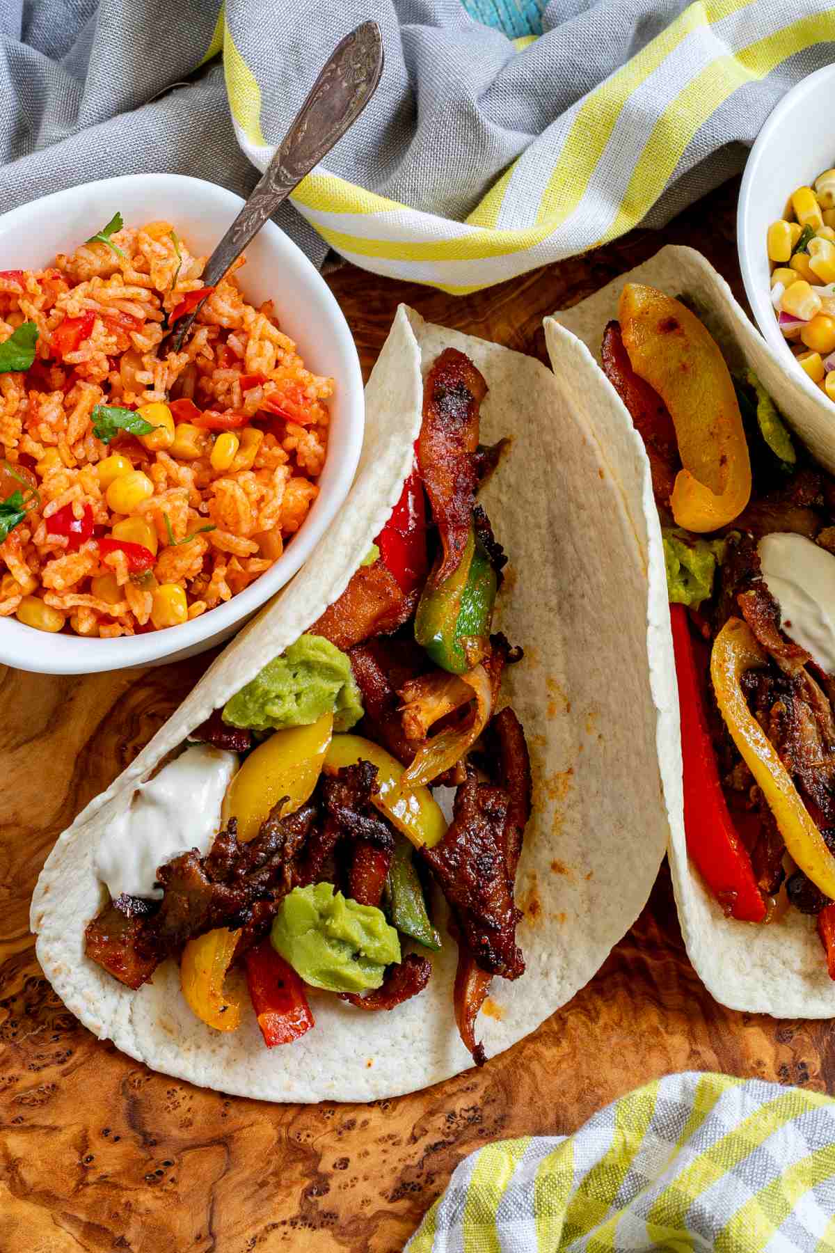 Small tortillas with colorful pepper slices and crispy brown mushroom shreds topped with white and green sauces on a wooden board. Surrounded by side dishes.