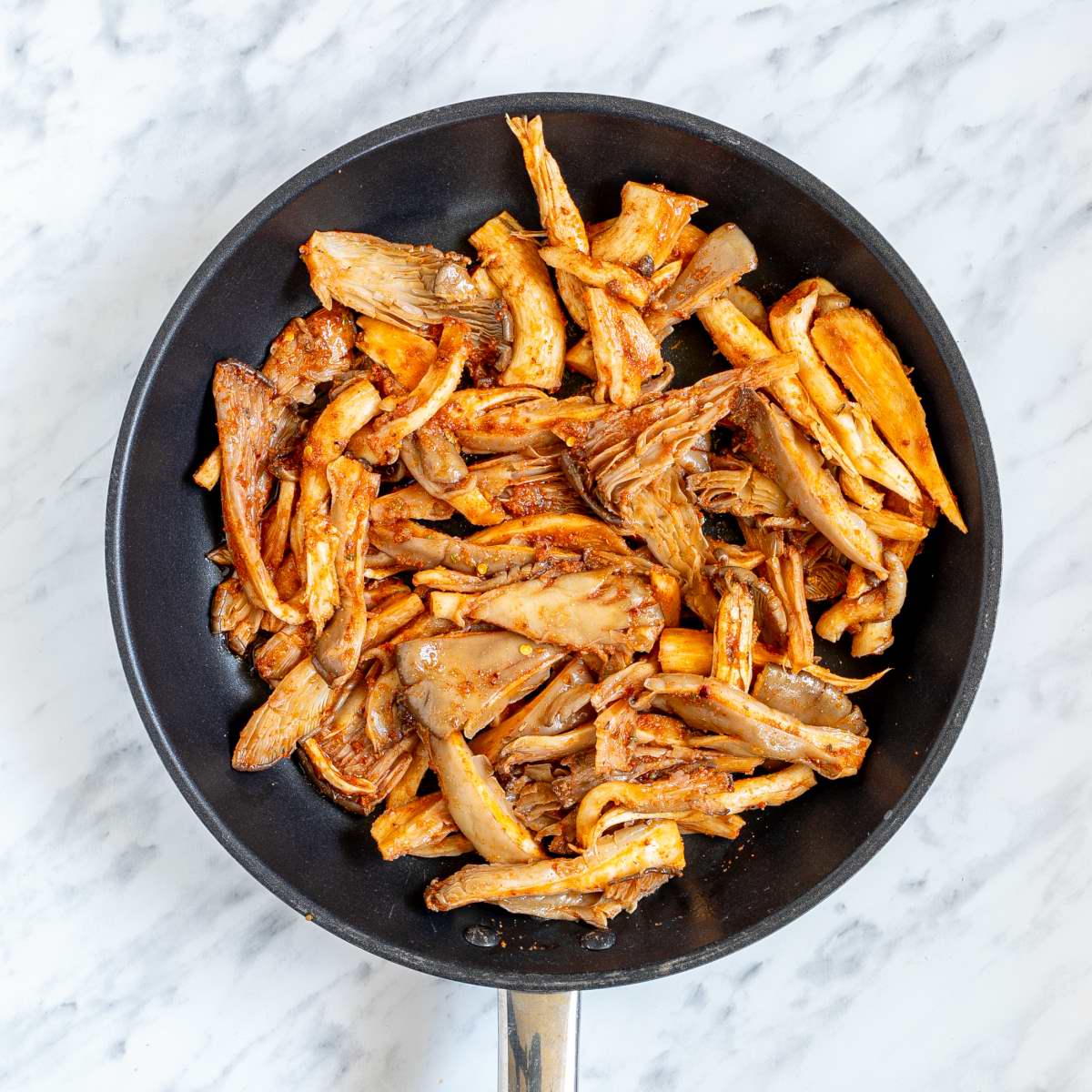 Marinated shredded mushrooms in a skillet.