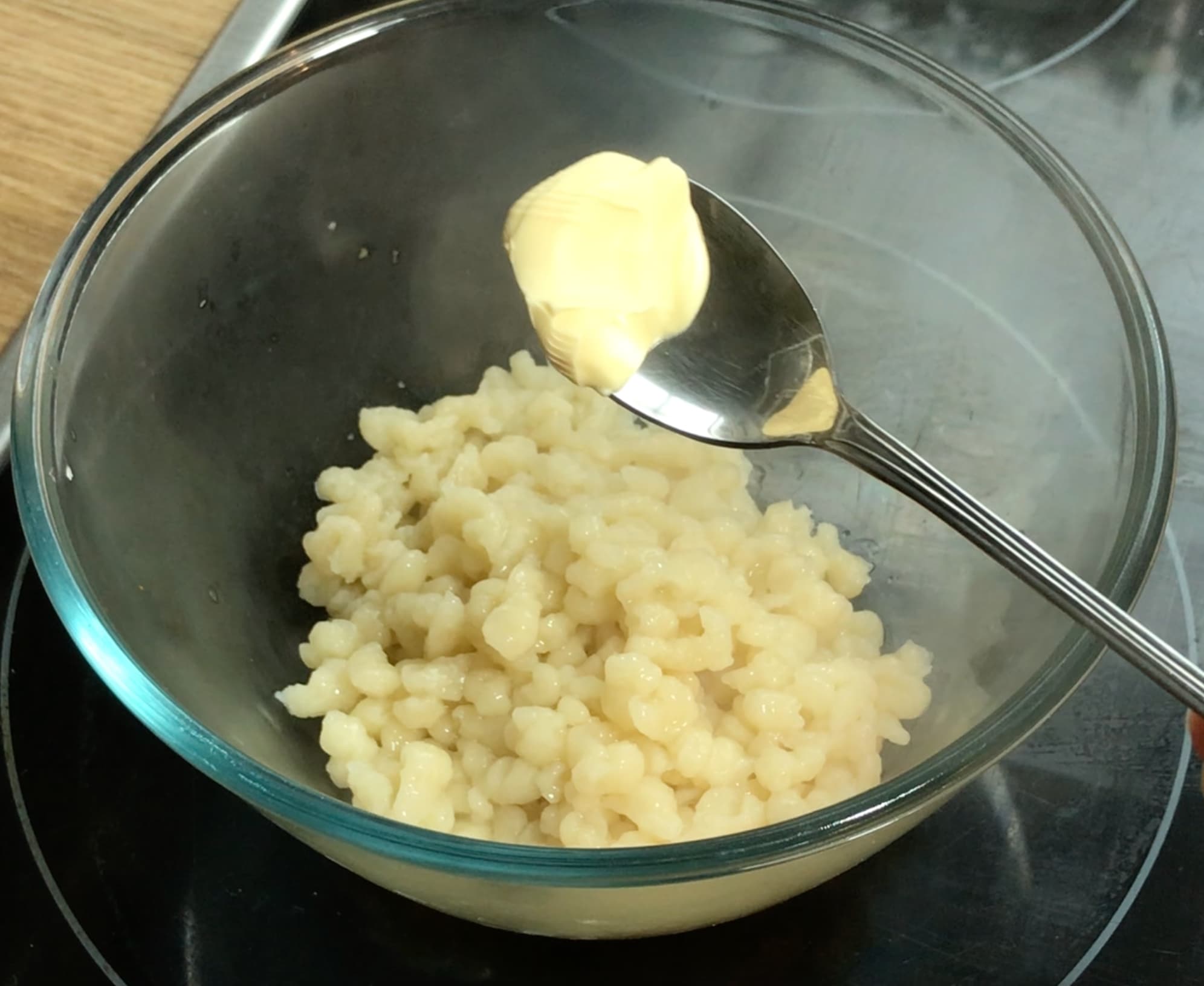 Small spoon with butter and tiny dumplings in a glass bowl.