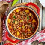 A pot of authentic Hungarian Goulash with meat and vegetables on a wooden table with two peppers on the side.