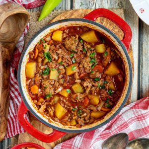 A pot of authentic Hungarian Goulash with meat and vegetables on a wooden table with two peppers on the side.