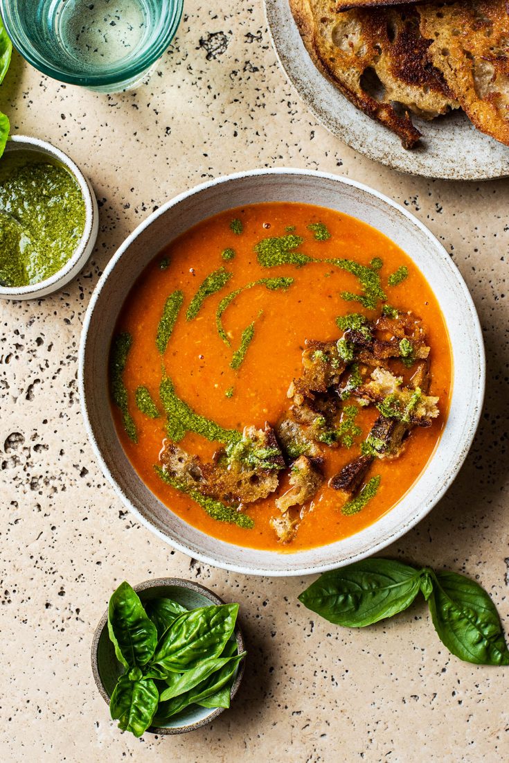 A bowl of tomato soup with rough croutons and pesto added. 
