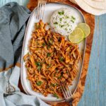Thin juicy golden brown oyster mushrooms shred sprinkled with chopped green herbs on a light blue tray served with a scoop of rice.