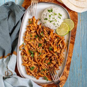 Thin juicy golden brown oyster mushrooms shred sprinkled with chopped green herbs on a light blue tray served with a scoop of rice.
