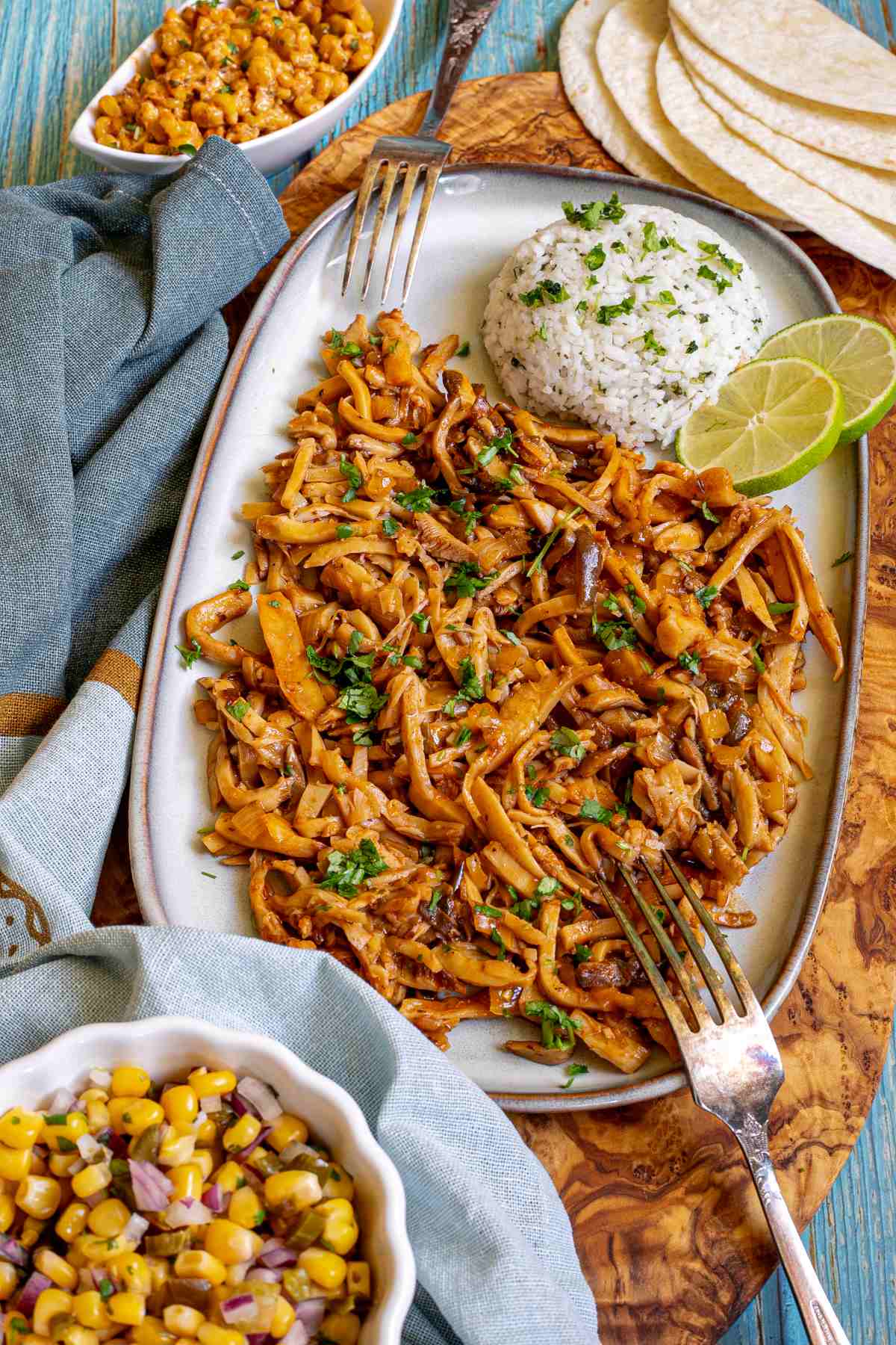 Thin juicy golden brown oyster mushrooms shred sprinkled with chopped green herbs on a light blue tray served with a scoop of rice.