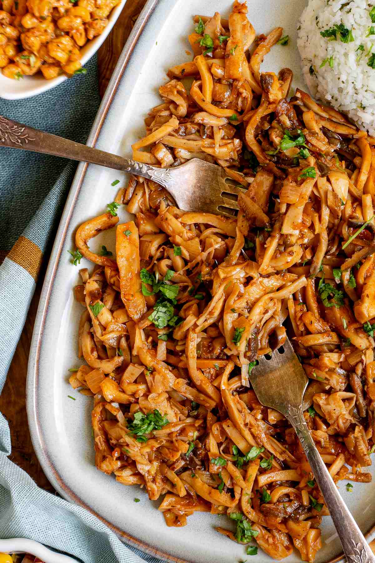 Thin juicy golden brown oyster mushrooms shred sprinkled with chopped green herbs on a light blue tray served with a scoop of rice.