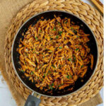 Black frying pan with thin juicy golden brown oyster mushrooms shred sprinkled with chopped green herbs.