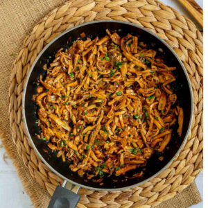 Black frying pan with thin juicy golden brown oyster mushrooms shred sprinkled with chopped green herbs.