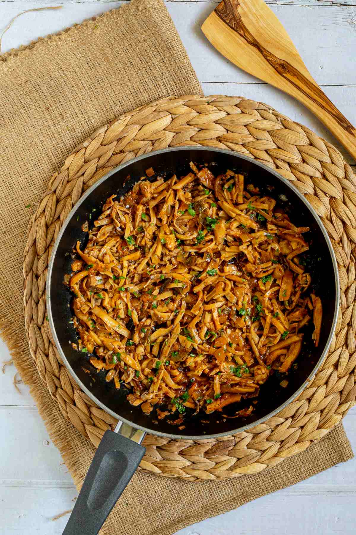 Black frying pan with thin juicy golden brown oyster mushrooms shred sprinkled with chopped green herbs. 