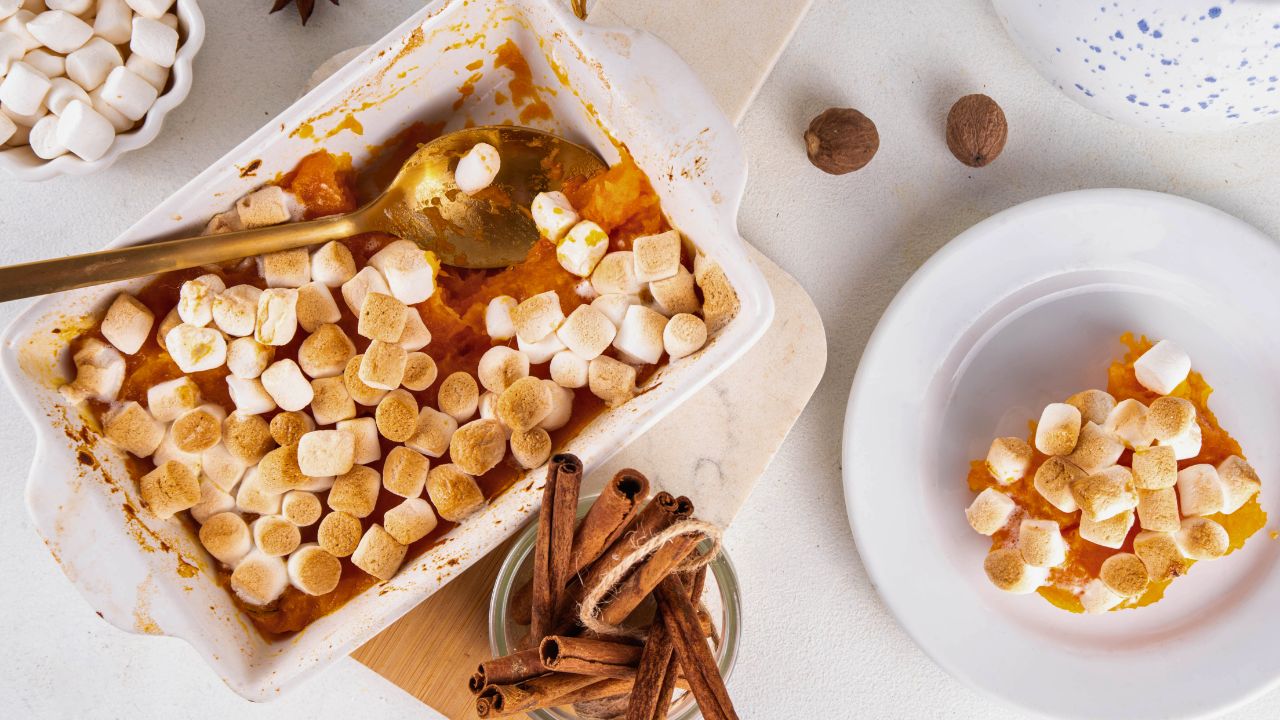 Baked sweet potato casserole topped with mini marshmallows in a dish and on a plate.