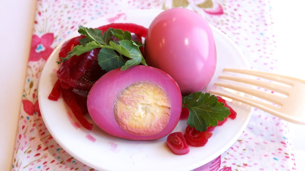 A plate of pink pickled eggs garnished with parsley on a floral tablecloth.