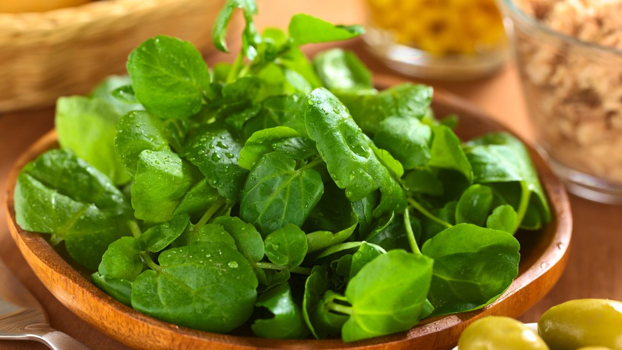 Fresh green salad leaves in a wooden bowl on a warm-toned table.