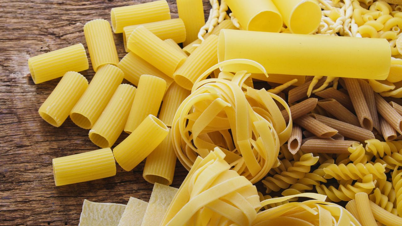 Assorted uncooked pasta shapes scattered on a rustic wooden surface.