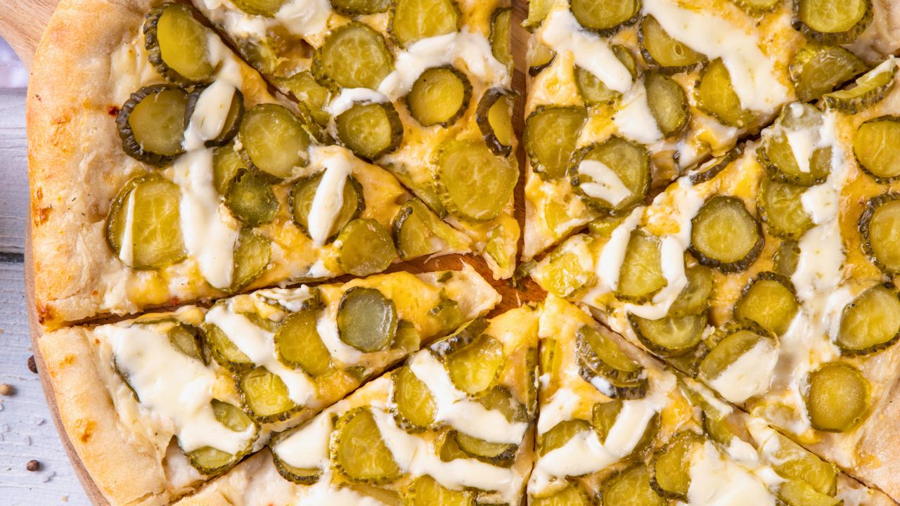 A pizza topped with sliced pickles and creamy sauce on a wooden surface.