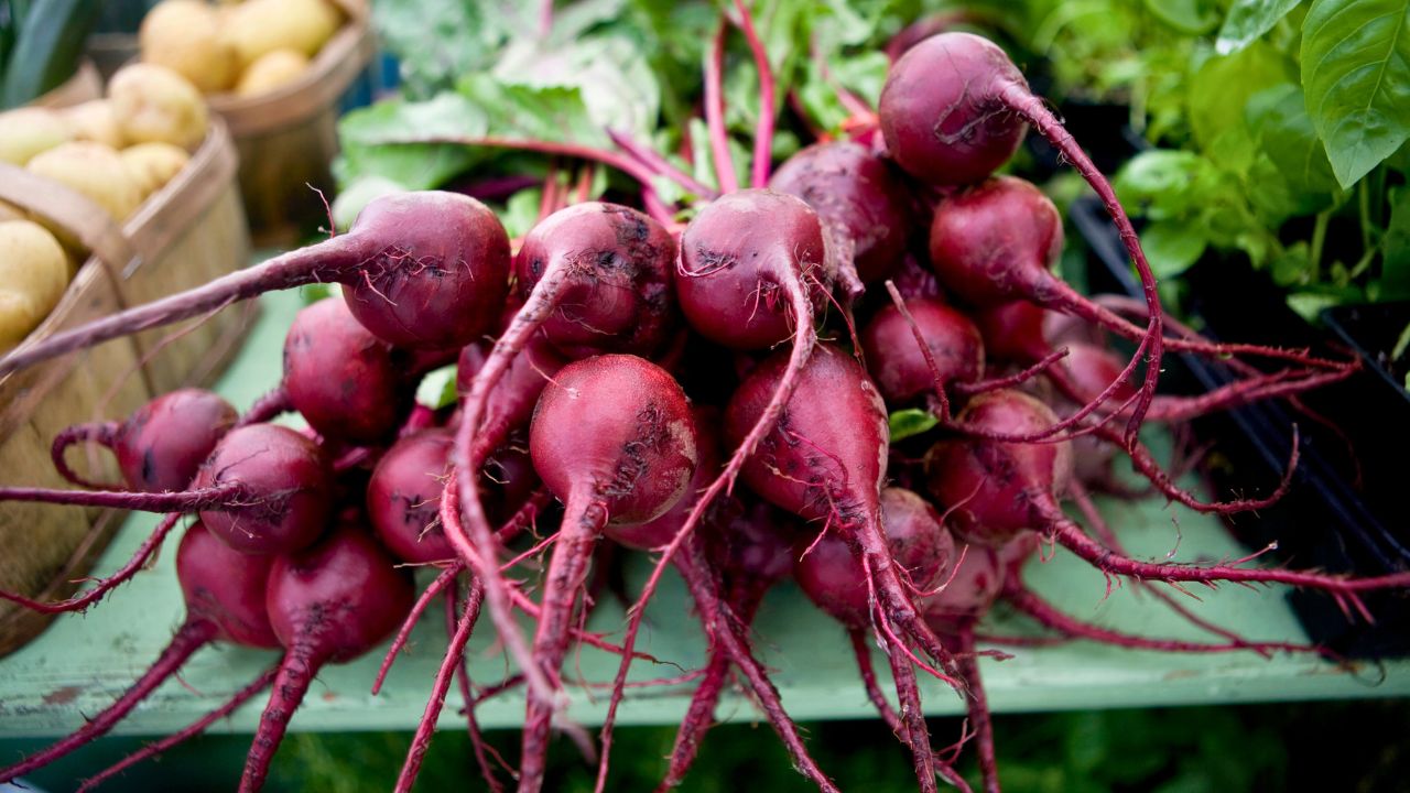 Fresh red beets with leafy tops piled on a market table.