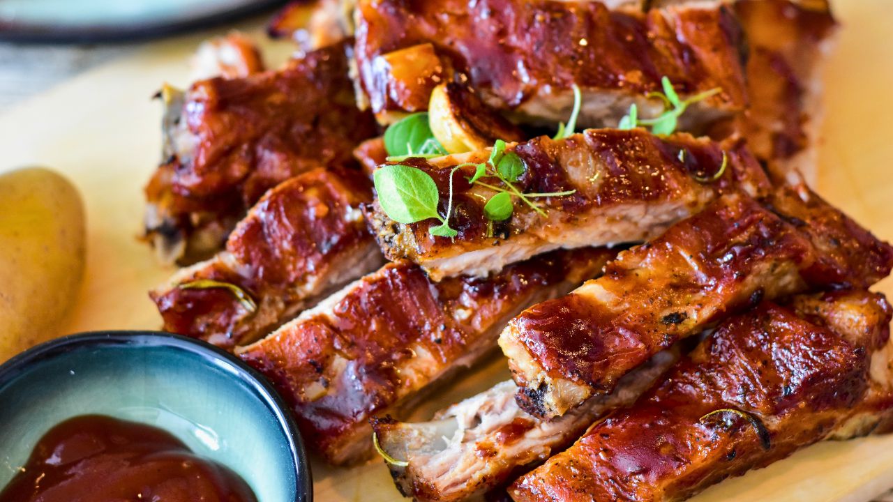 Glazed grilled ribs on a plate with dipping sauce and a potato.