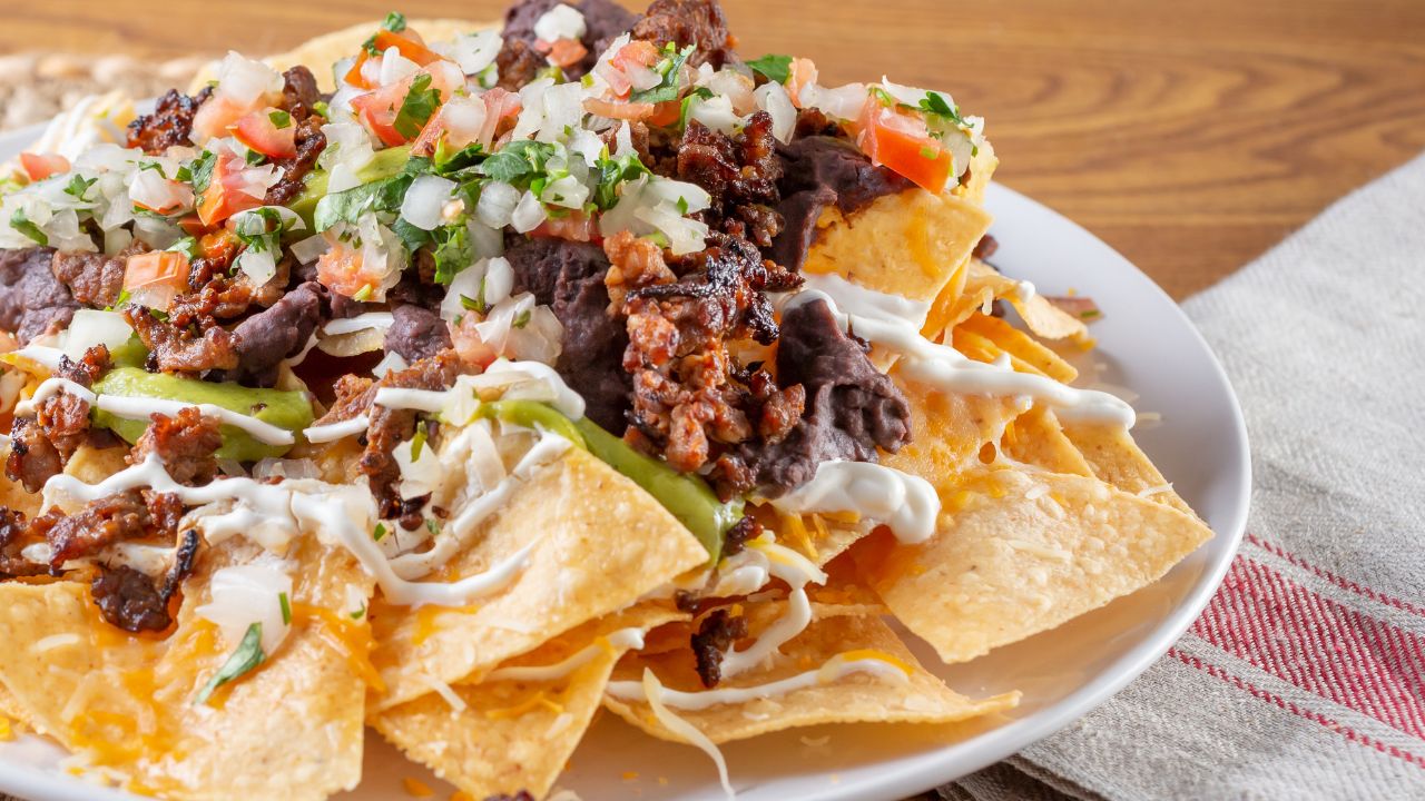 A plate of loaded nachos topped with cheese, beans, sour cream, tomatoes, and cilantro.
