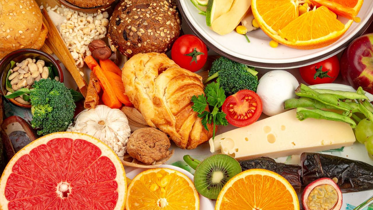 An overhead arrangement of fruits, vegetables, bread, cheese, and nuts on a table.