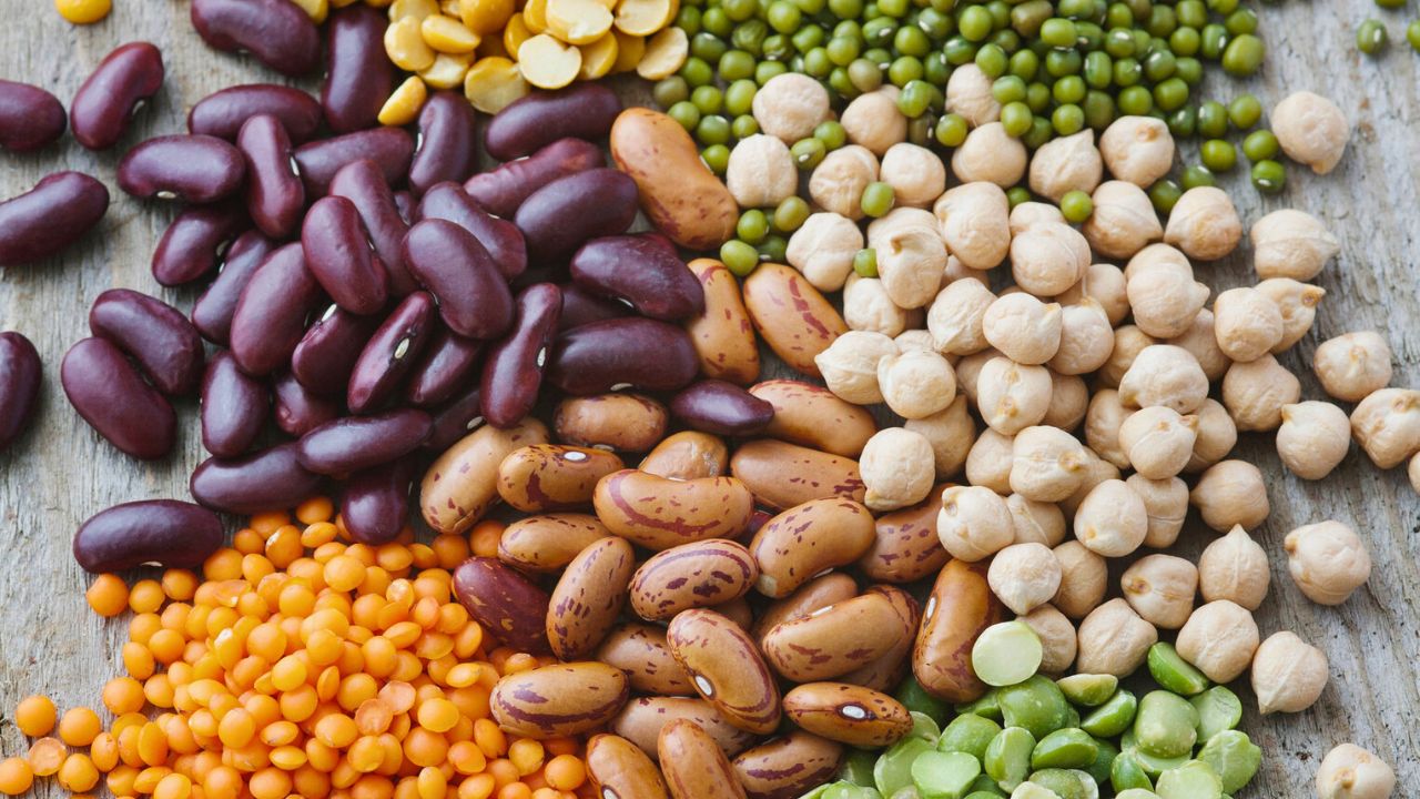 Assorted dried beans, lentils, peas, and chickpeas arranged on a wooden surface.