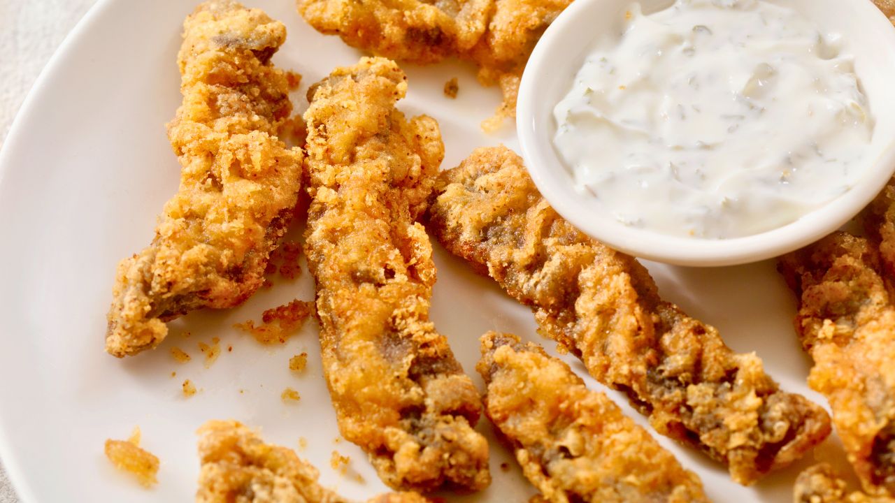 Golden fried chicken strips on a white plate with a small bowl of dipping sauce.