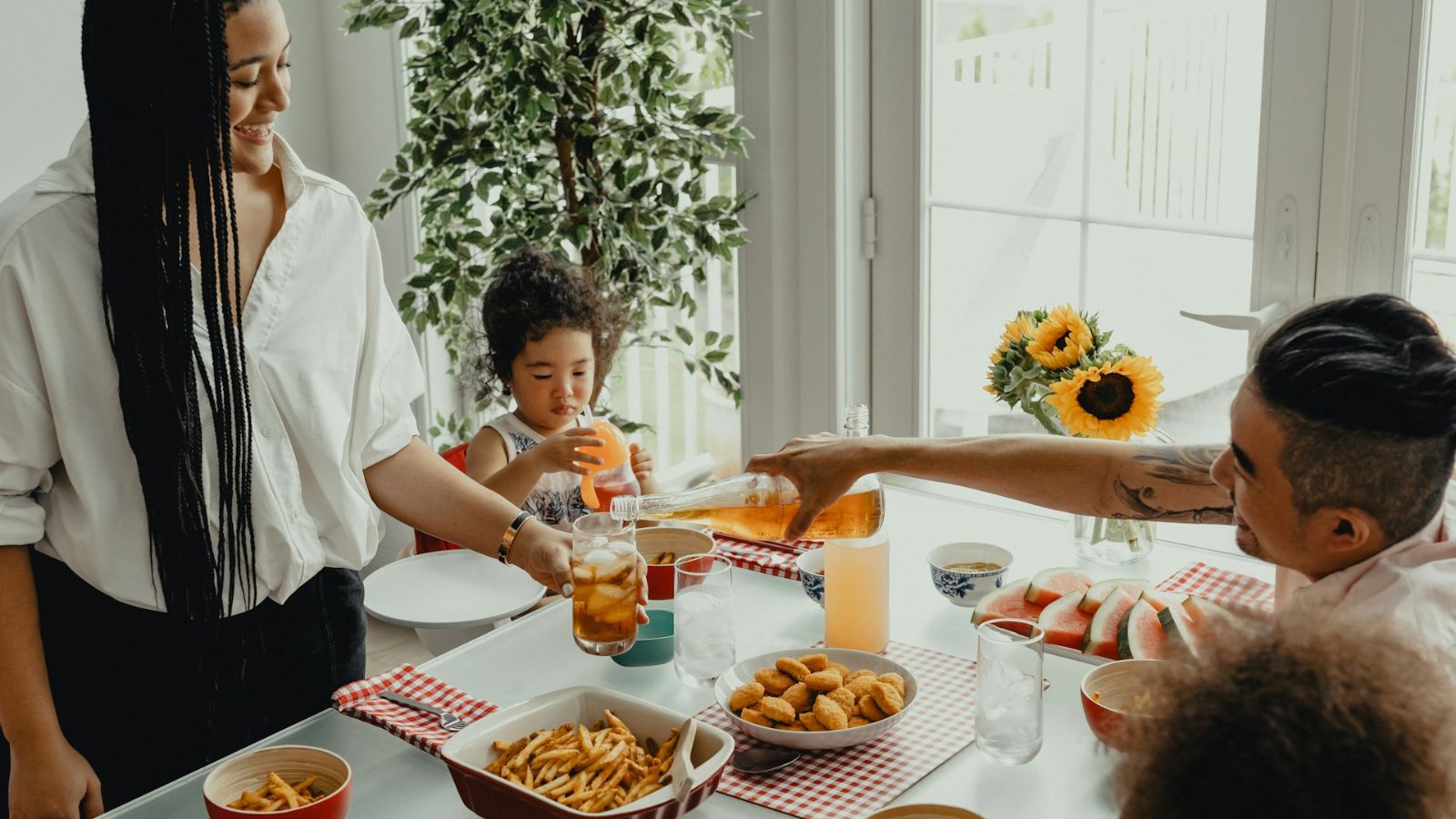 A family shares food and drinks around a dining table in a bright home.