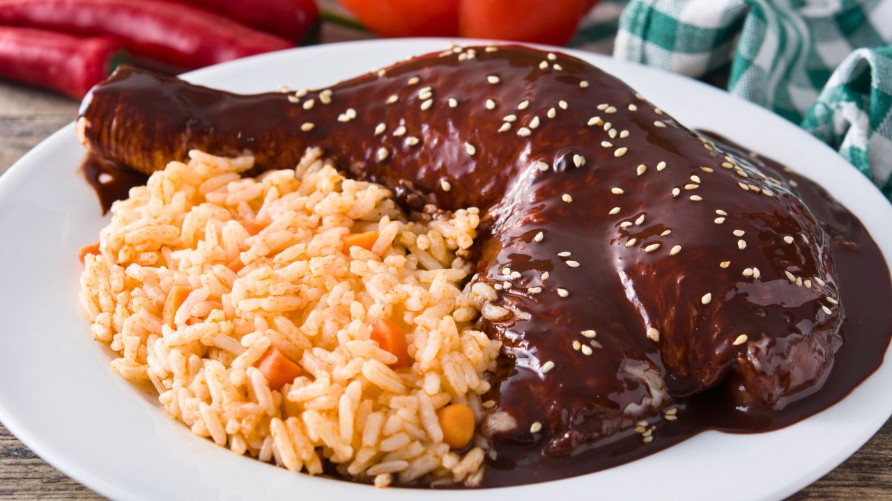 A saucy chicken leg served with seasoned rice on a white plate.