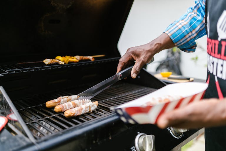 A person grilling bacon-wrapped hotdogs outdoors, highlighting summer BBQ fun.