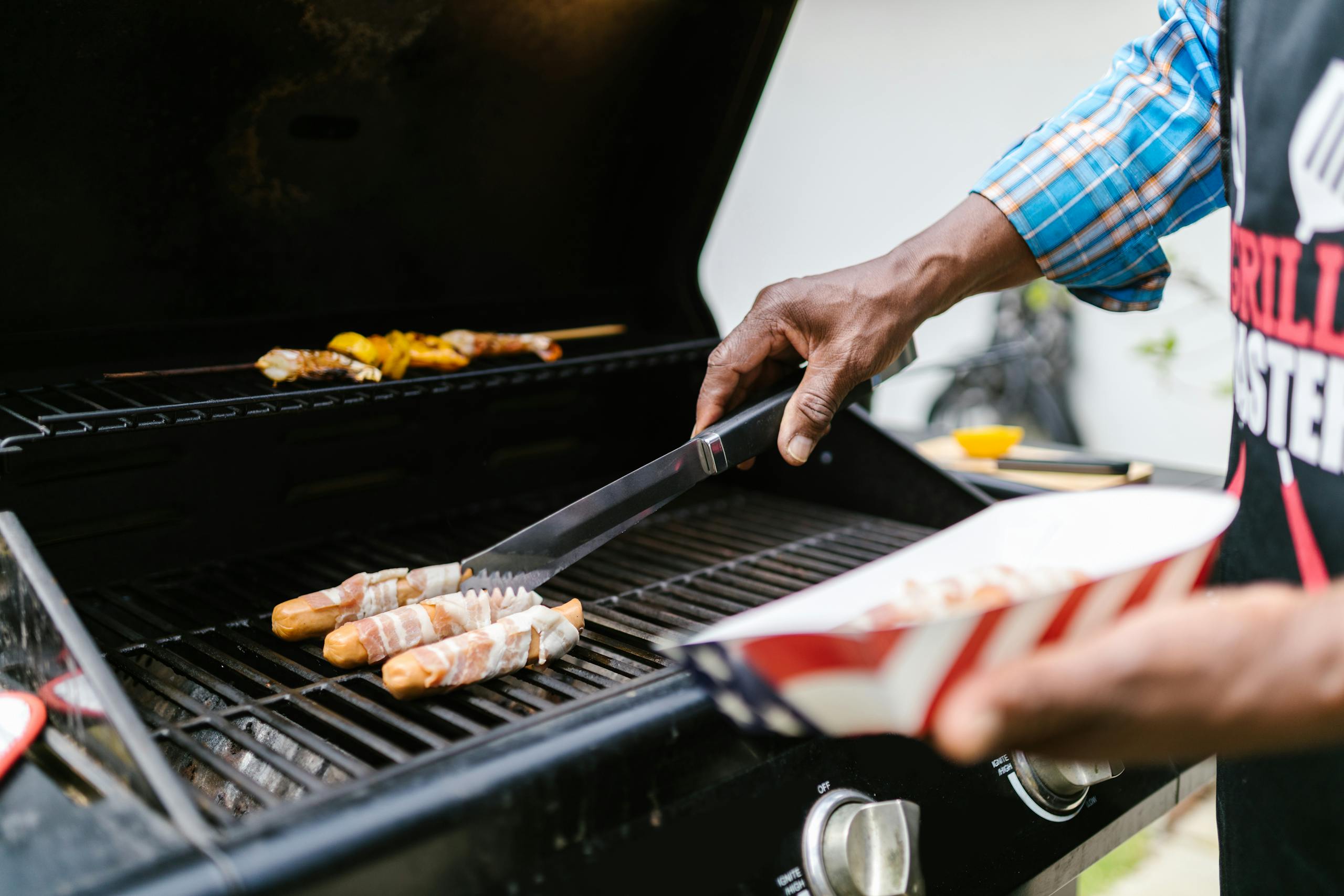 A person grilling bacon-wrapped hotdogs outdoors, highlighting summer BBQ fun.