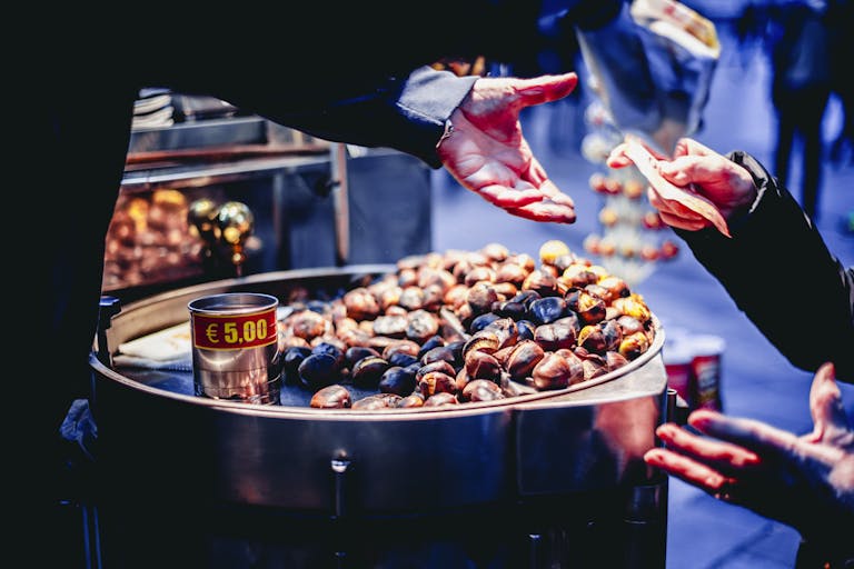 A street vendor selling roasted chestnuts to a customer on a lively outdoor market.