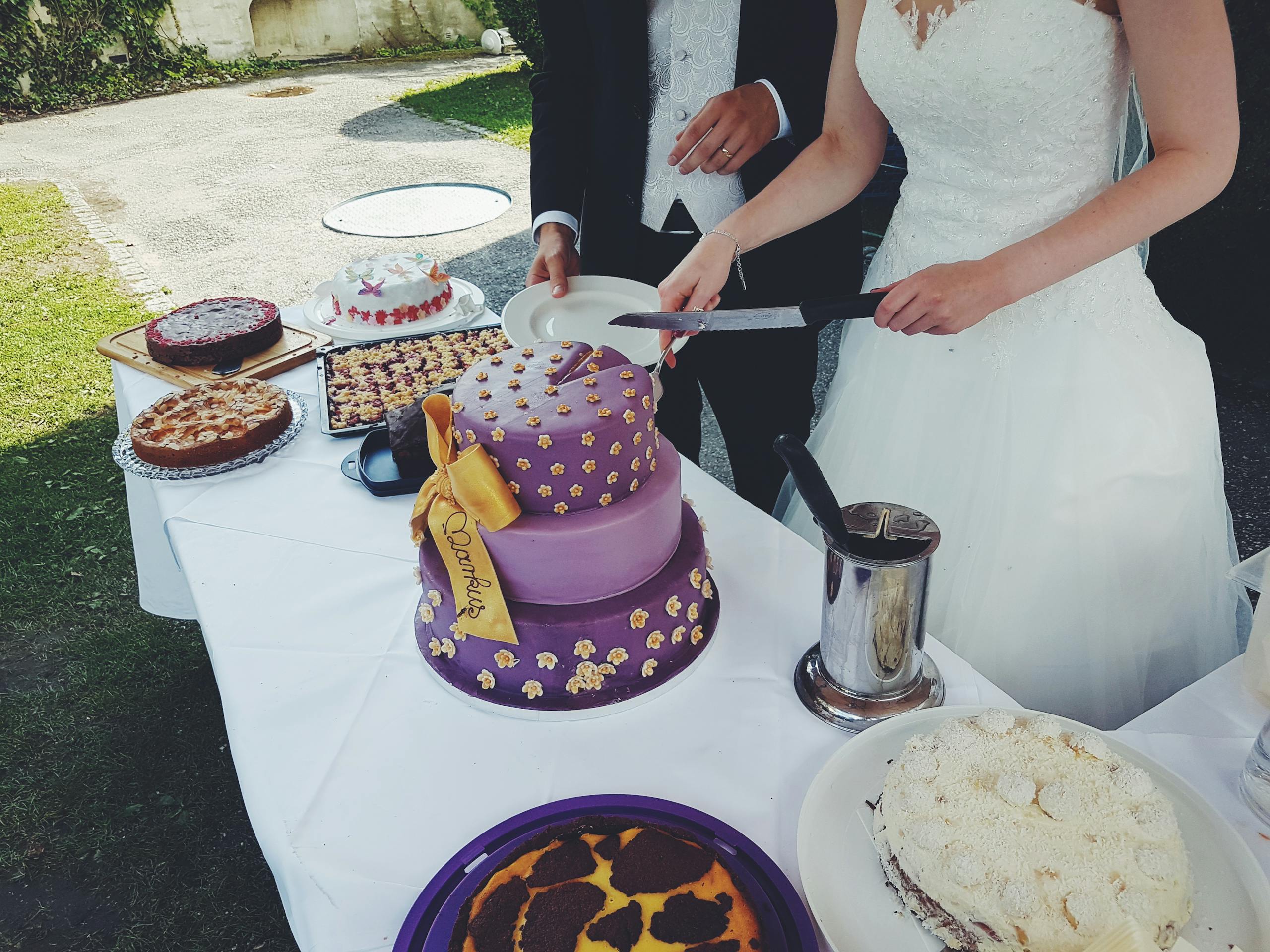 Bride and groom cutting a purple wedding cake at an outdoor celebration.