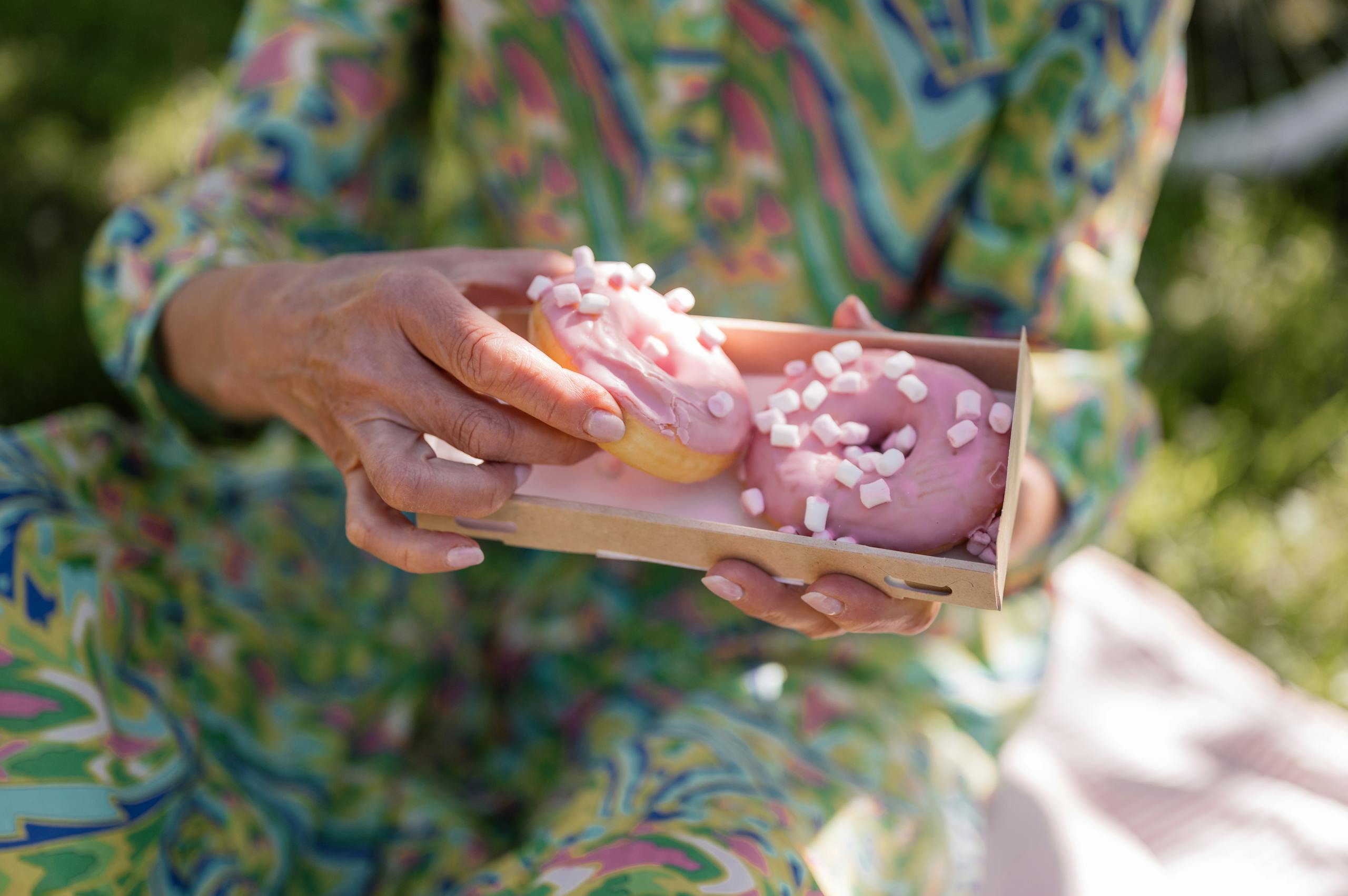 Close-up of a woman holding pink donuts at a picnic with floral attire.